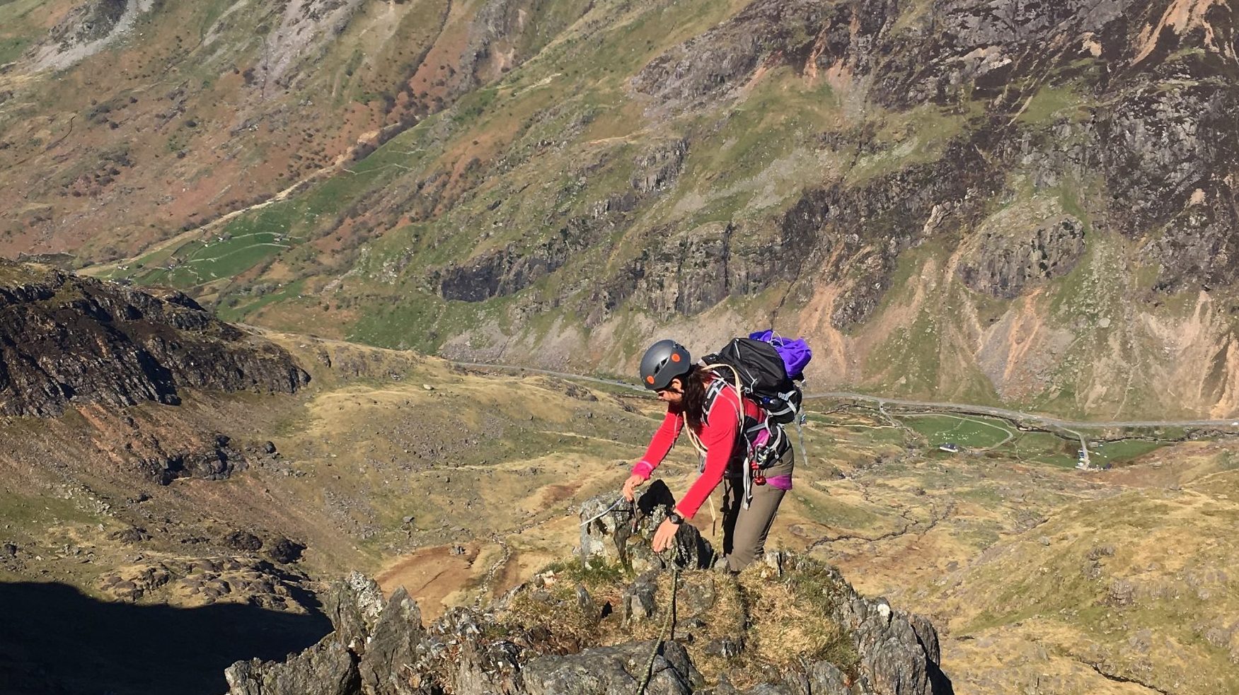 A mountaineer reaches the crest of the ridge of the Clogwyn y Person Arete with Llanberis Pass below during a summer mountaineering course in Snowdonia