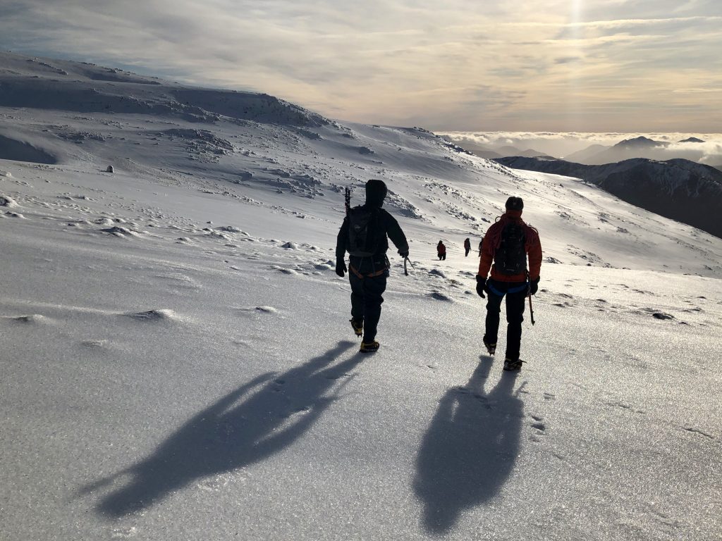 Two climbers begin their descent from Ben Nevis towards the setting sun after climbing Ledge Route on a winter mountaineering course