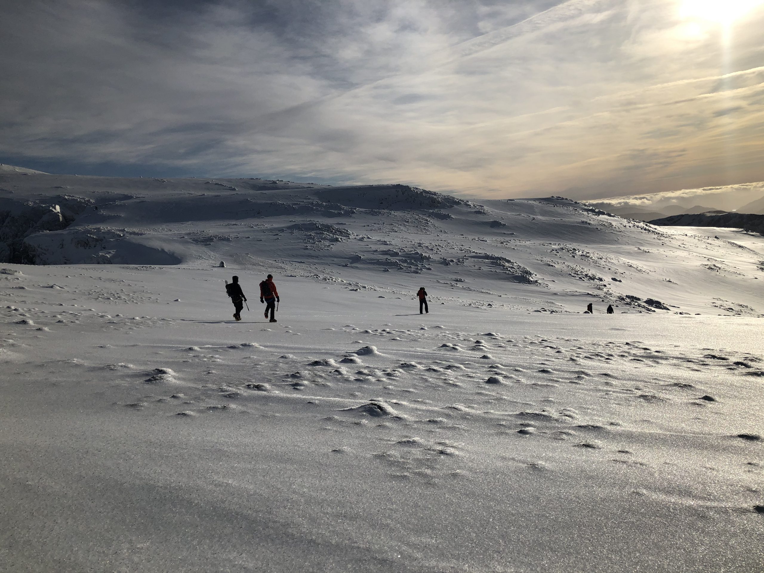 A group of mountaineers descending the summit plateau of Ben Nevis in winter, with the snow sparkling all around them