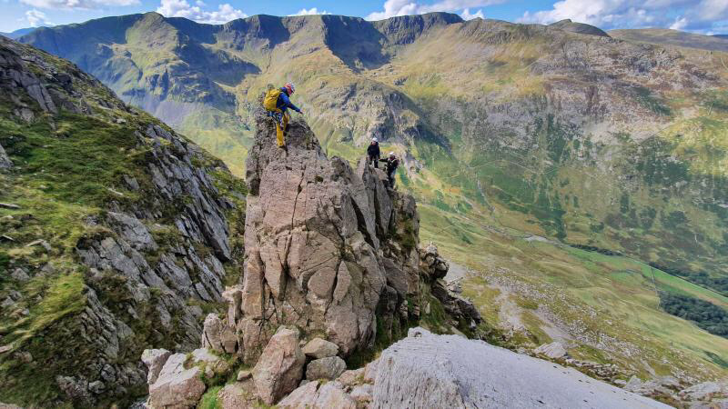 Three climbers negotiating the pinnacles on Pinnacle Ridge, St Sunday Crag, with amazing views of Helvellyn in the background