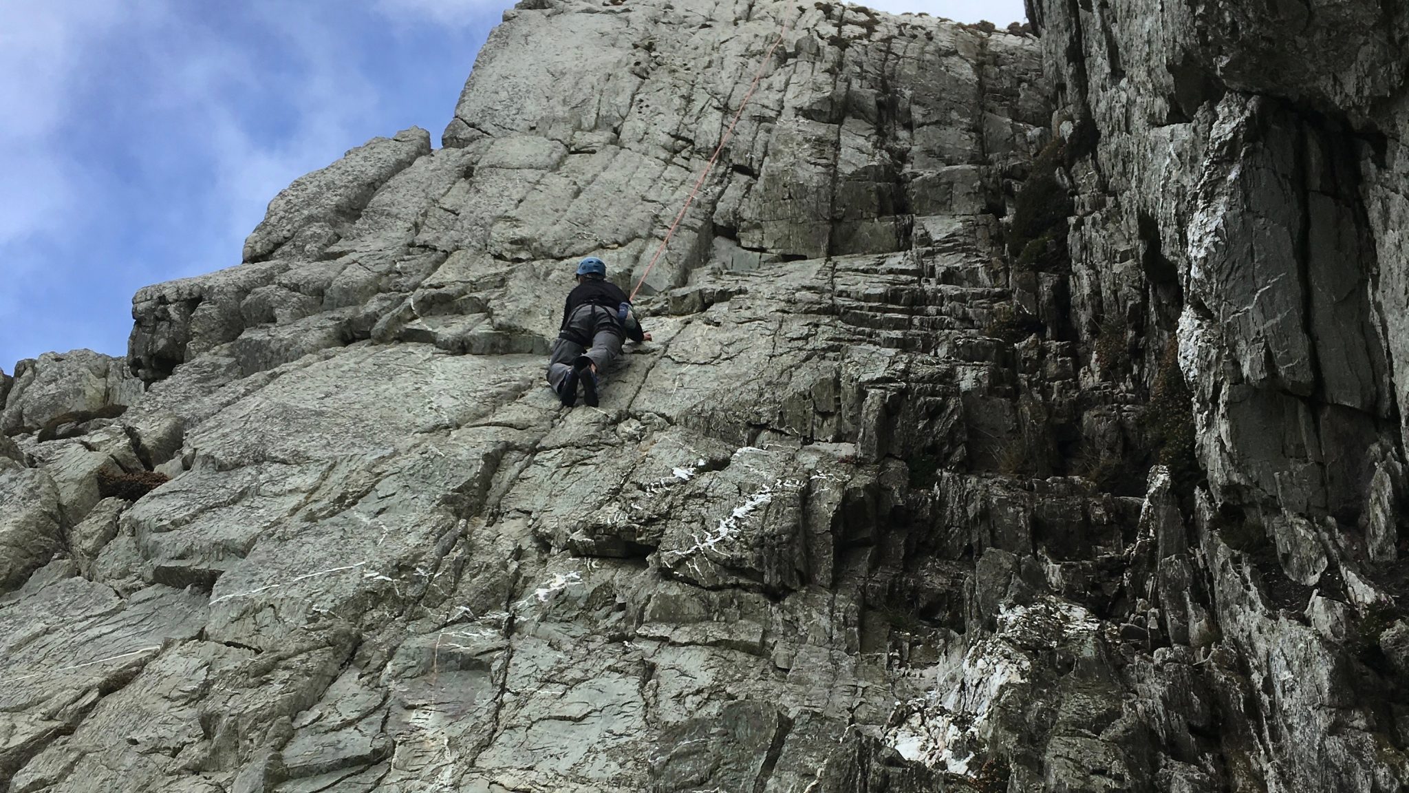 A rock climber considering his next move on a climb on Anglesey, North Wales