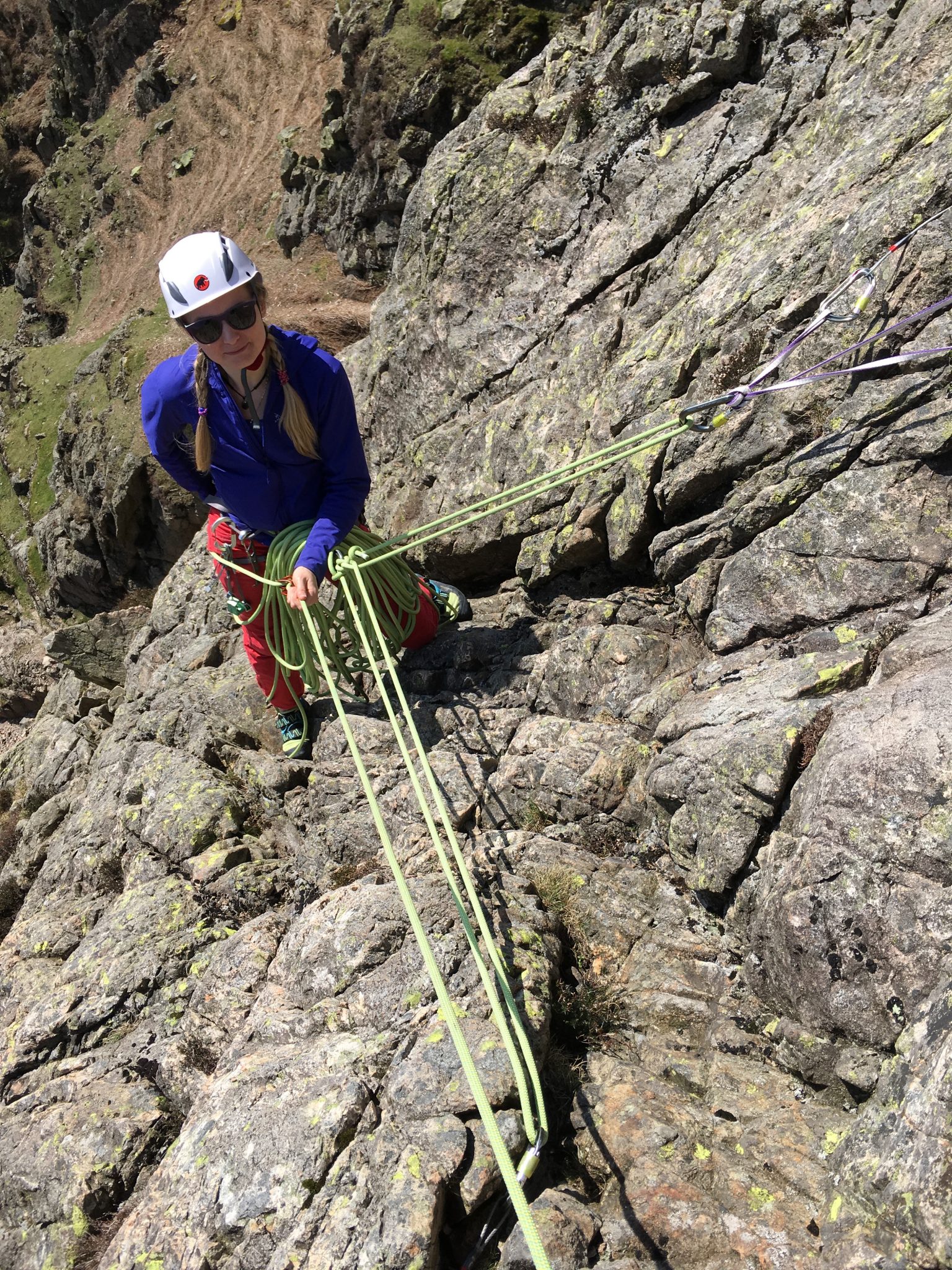 A rock climber securely anchored to the rock at her belay on a multi-pitch rock climbing course in the Lake District
