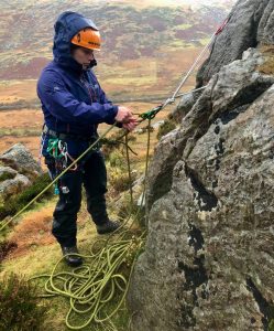 A climber learns how to belay herself and her partner and uses an Italian Hitch during a lead scrambling course in Snowdonia