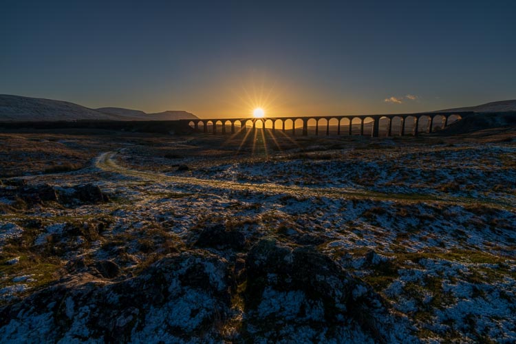 The setting sun's rays burst under the arches of Ribblehead Viaduct, a highlight of the Yorkshire Three Peaks Challenge